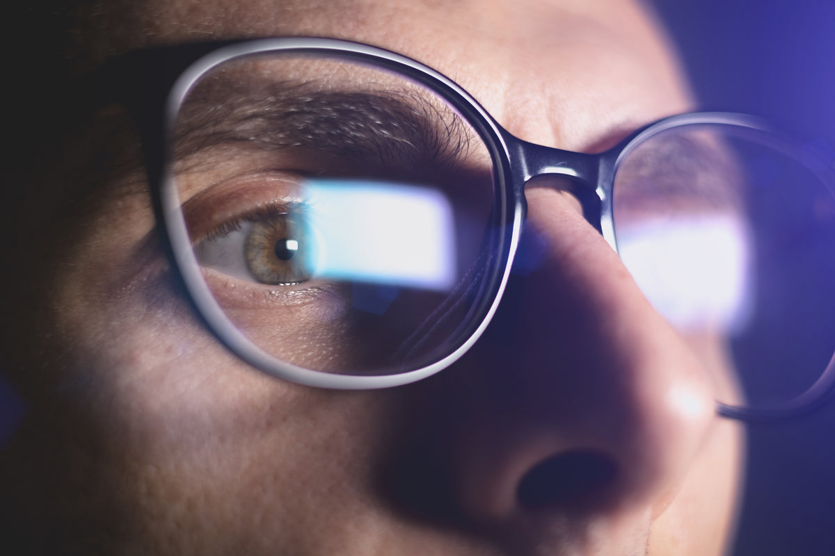 Close-up of a person wearing glasses with a blurred screen reflection.
